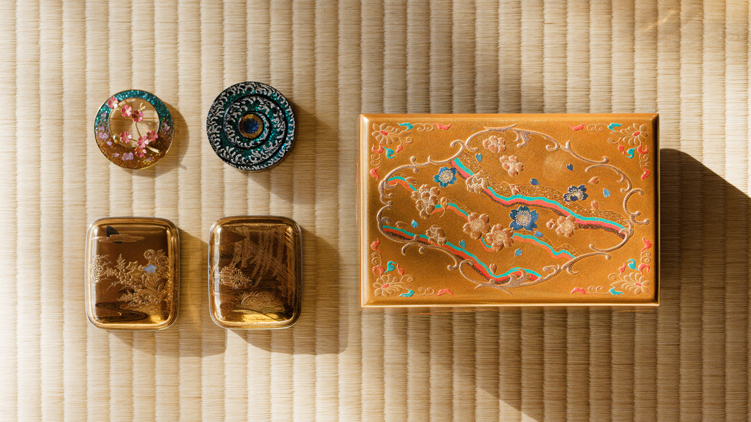 Photo A selection of maki-e pieces by Isshu Tamura. From top left: brooch with floral motifs, maki-e incense holder with gold spiral, maki-e treasure box (small)