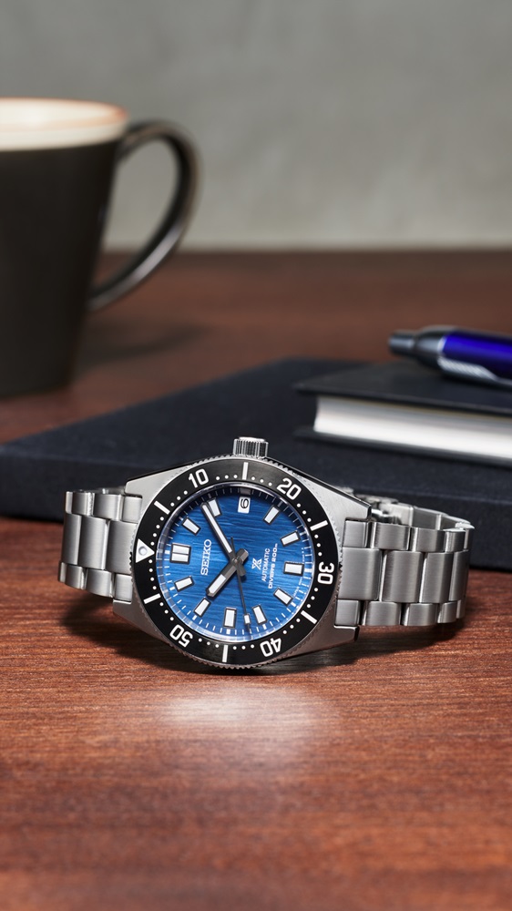 Relógio automático Seiko Prospex, Reinterpretação Moderna do Diver's de 1965, Edição Especial Save the Ocean. Relógio de mergulho em aço com mostrador azul sobre mesa de madeira.