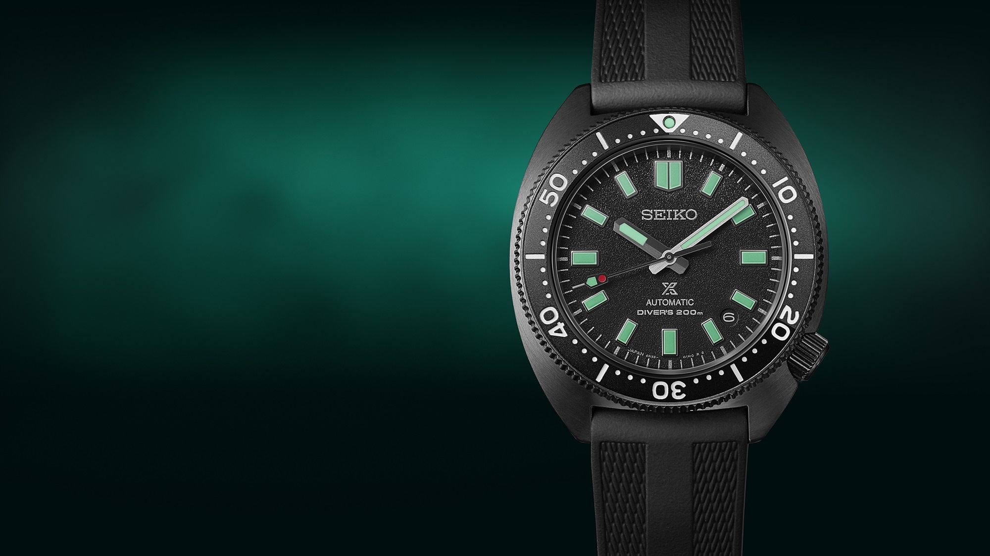 Detalhe do relógio de mergulho Seiko Prospex Diver's The Black Series Night Vision de edição limitada, SPB335J1, modelo preto com detalhes em verde-água luminescentes. Foto do relógio sobre fundo preto e verde esmeralda.