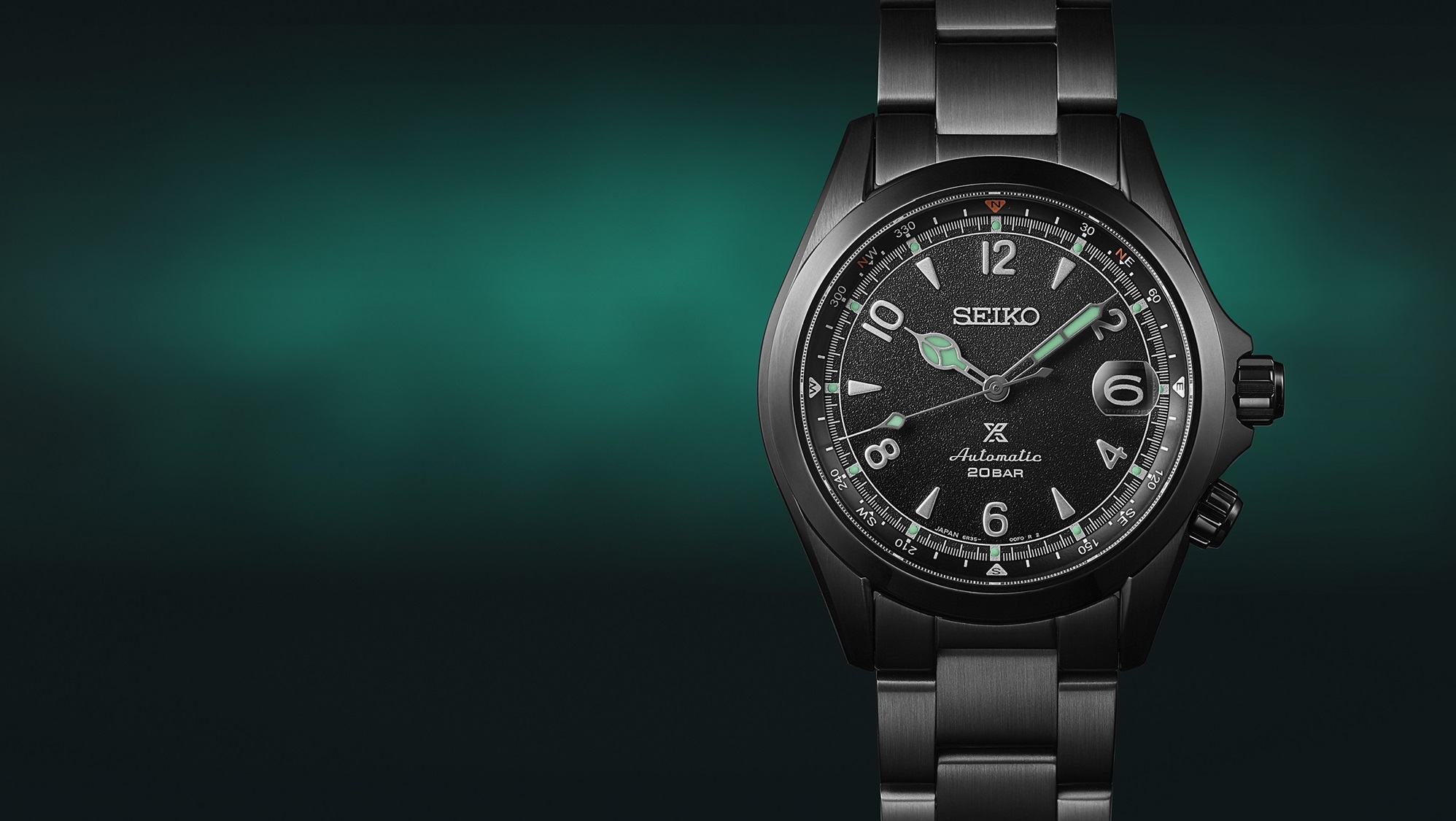 Detalhe do mostrador do relógio mecânico Seiko Prospex Alpinist, edição limitada The Black Series Night Vision, sobre um fundo verde-esmeralda e preto.