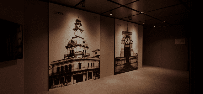 Detalhe de exposição sobre a Seiko, com fotografias a preto e branco em grande escala de edifícios importantes para a história da marca, como o Wako e a torre do relógio em Ginza.