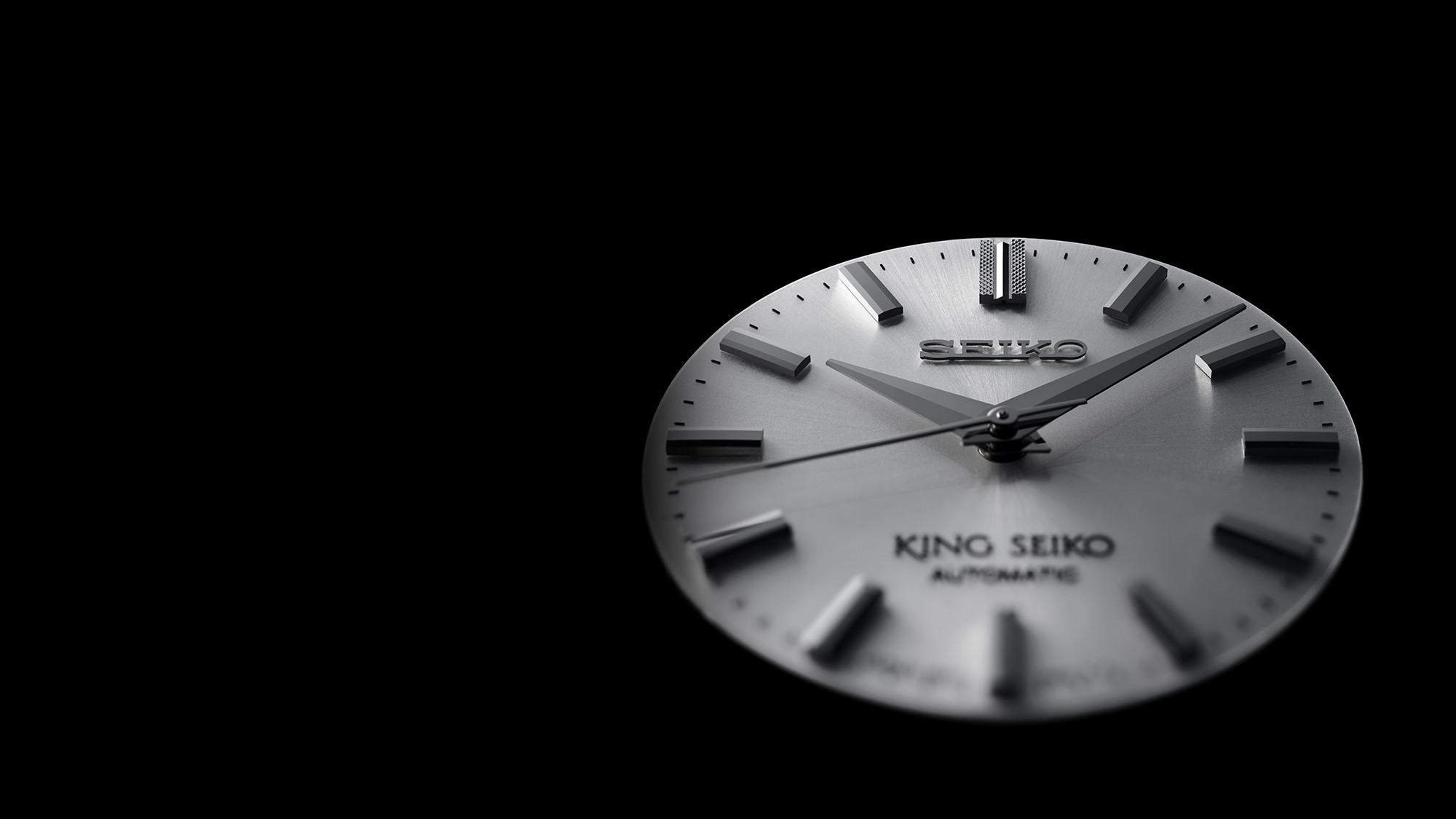 Fotografia em perspectiva da placa metálica do mostrador com os ponteiros e os índices já aplicados de um relógio mecânico King Seiko.