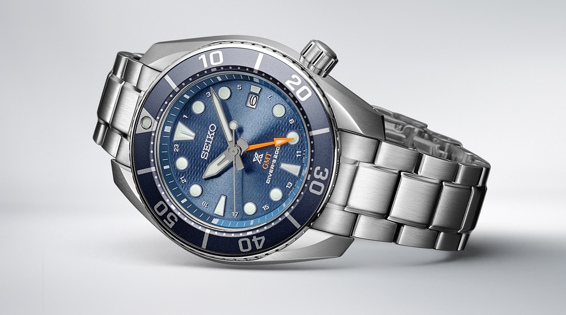 Fotografia do relógio de mergulho Seiko Prospex Sumo GMT em azul, deitado sobre um cenário cinzento claro.