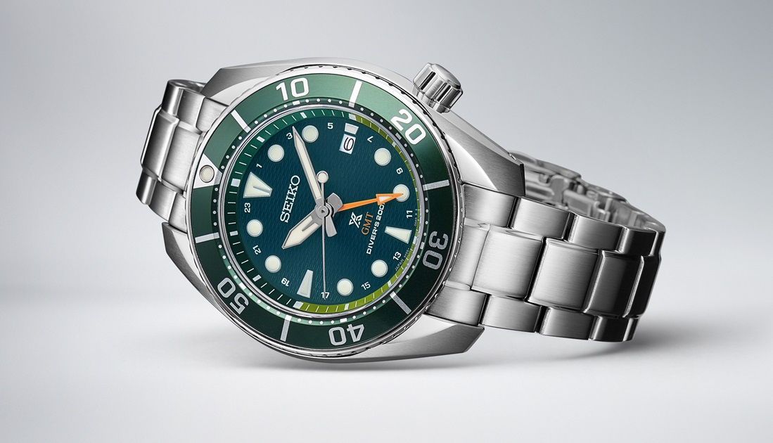 Fotografia do relógio de mergulho Seiko Prospex Sumo GMT em verde, deitado sobre um cenário cinzento claro.